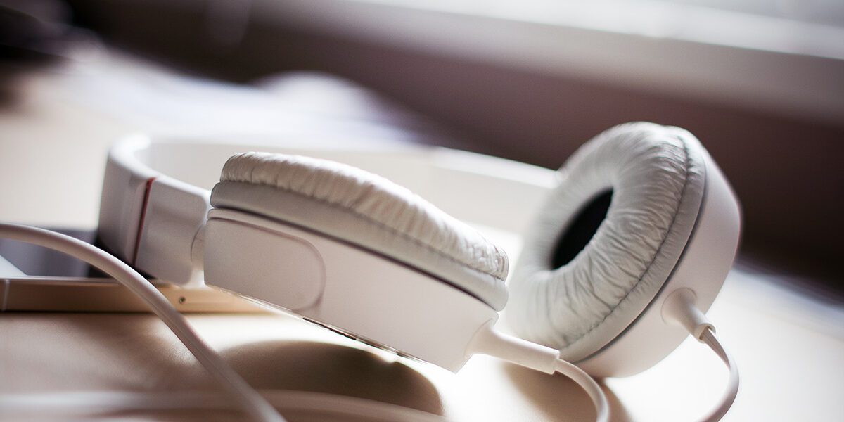 White over-ear headphones resting on a wooden surface near a window.