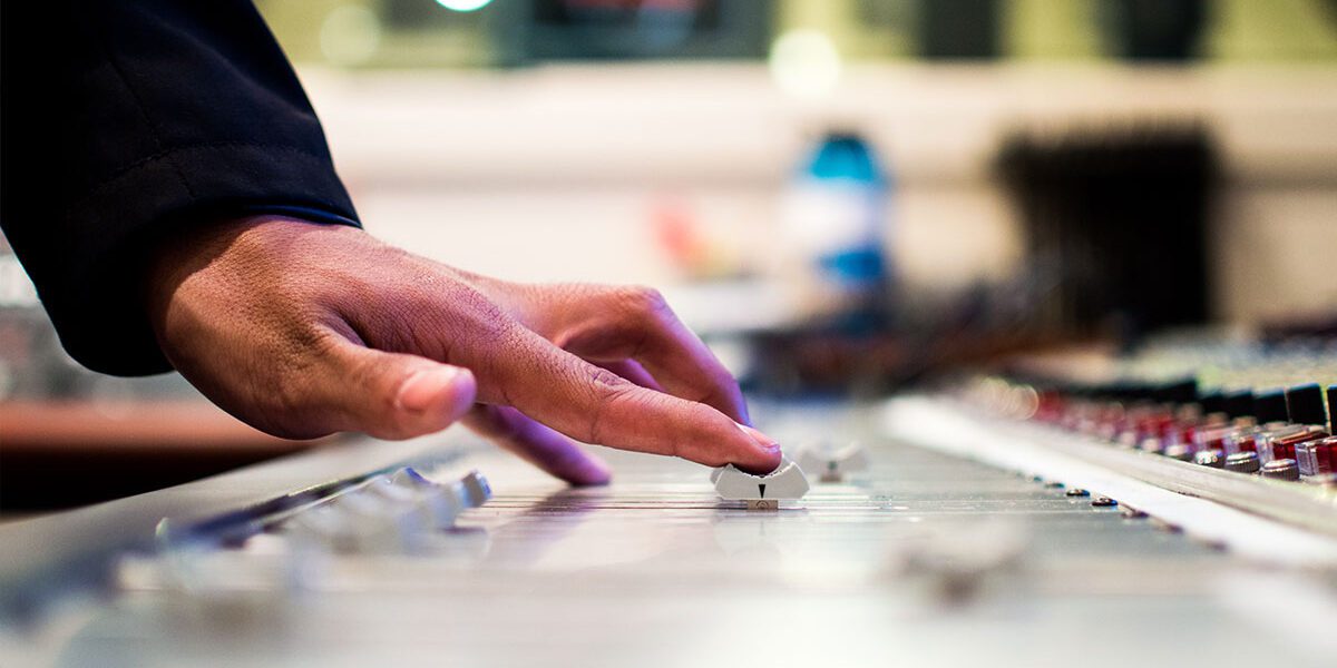 Close-up of hands adjusting audio mixer controls in a studio.